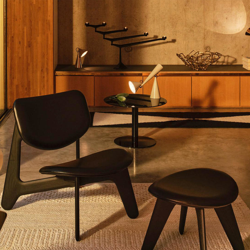 Elegant black-leather chair and stool on textured white rug, surrounded by warm wood and sleek black accents.