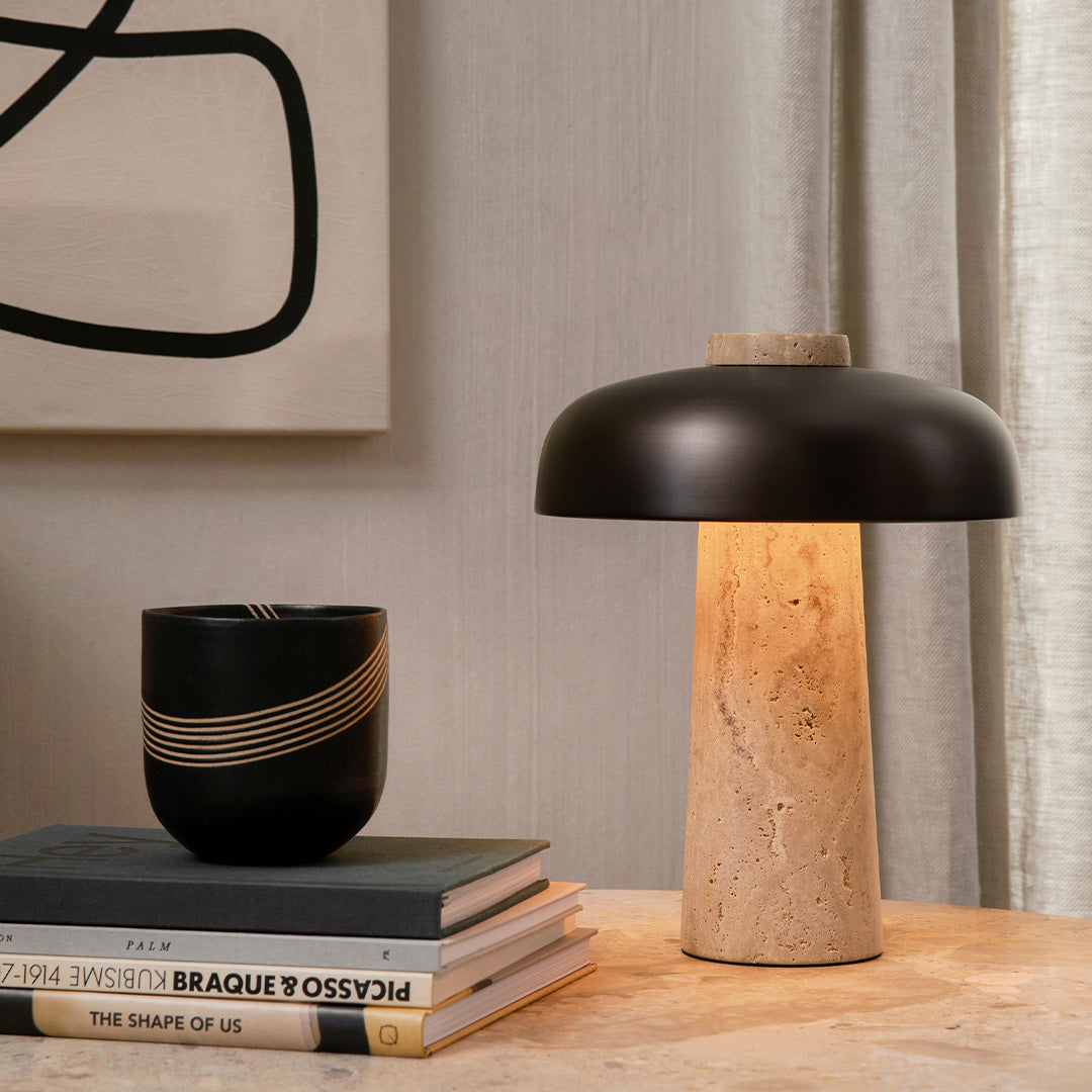 Black and beige lamp with a smooth finish; striped black vase; layered book stack on wooden table.