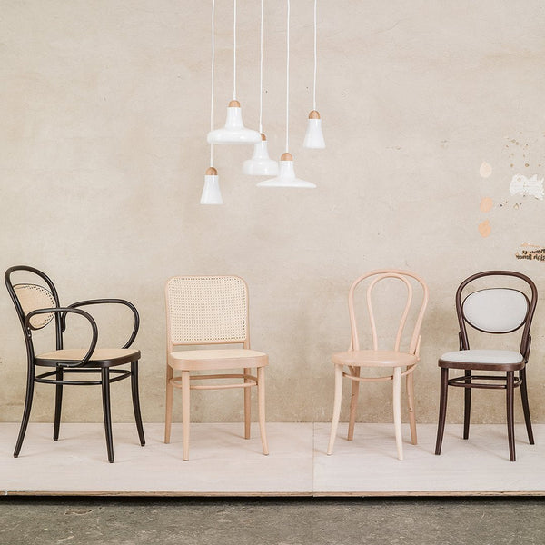 Four chairs in black, natural wood, and dark brown with curved backs; minimalist design against a neutral backdrop.