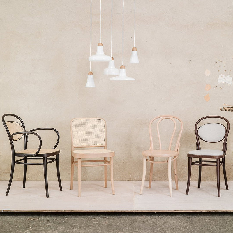 Four chairs in black, natural wood, and dark brown with curved backs; minimalist design against a neutral backdrop.