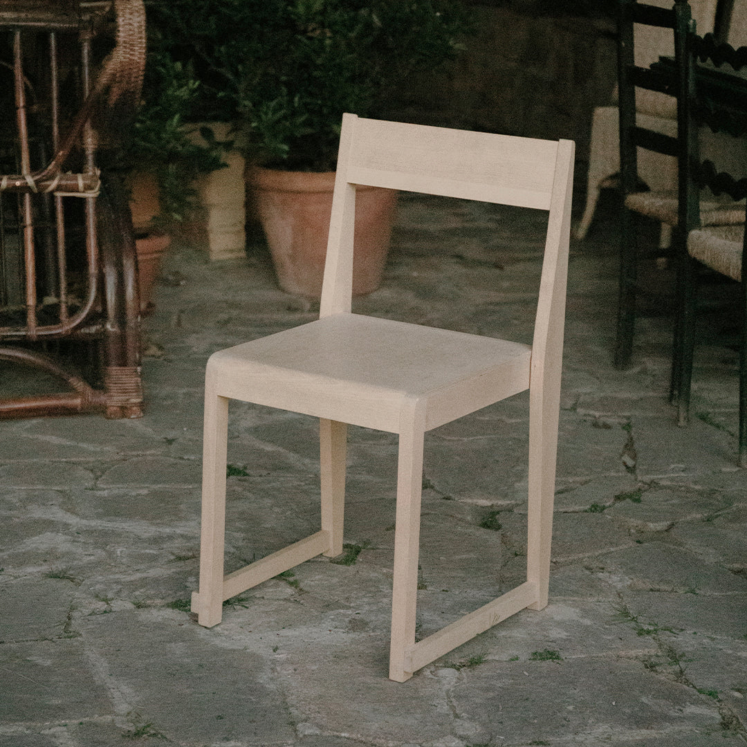 Light beige wooden chair with a minimalistic design, showcasing a smooth, unadorned finish against a stone backdrop.