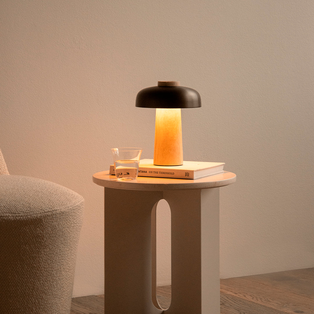 Modern lamp with a black top, warm amber glow, and a beige base, paired with a minimalist table and soft textures.