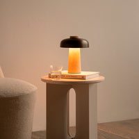 Modern lamp with a black top, warm amber glow, and a beige base, paired with a minimalist table and soft textures.