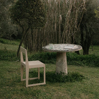 "Natural stone table with a circular patterned top in earthy tones, paired with a minimalist light wood chair."