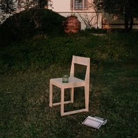 Minimalist white wooden chair on grass, showcasing a simple, modern design with clean lines.