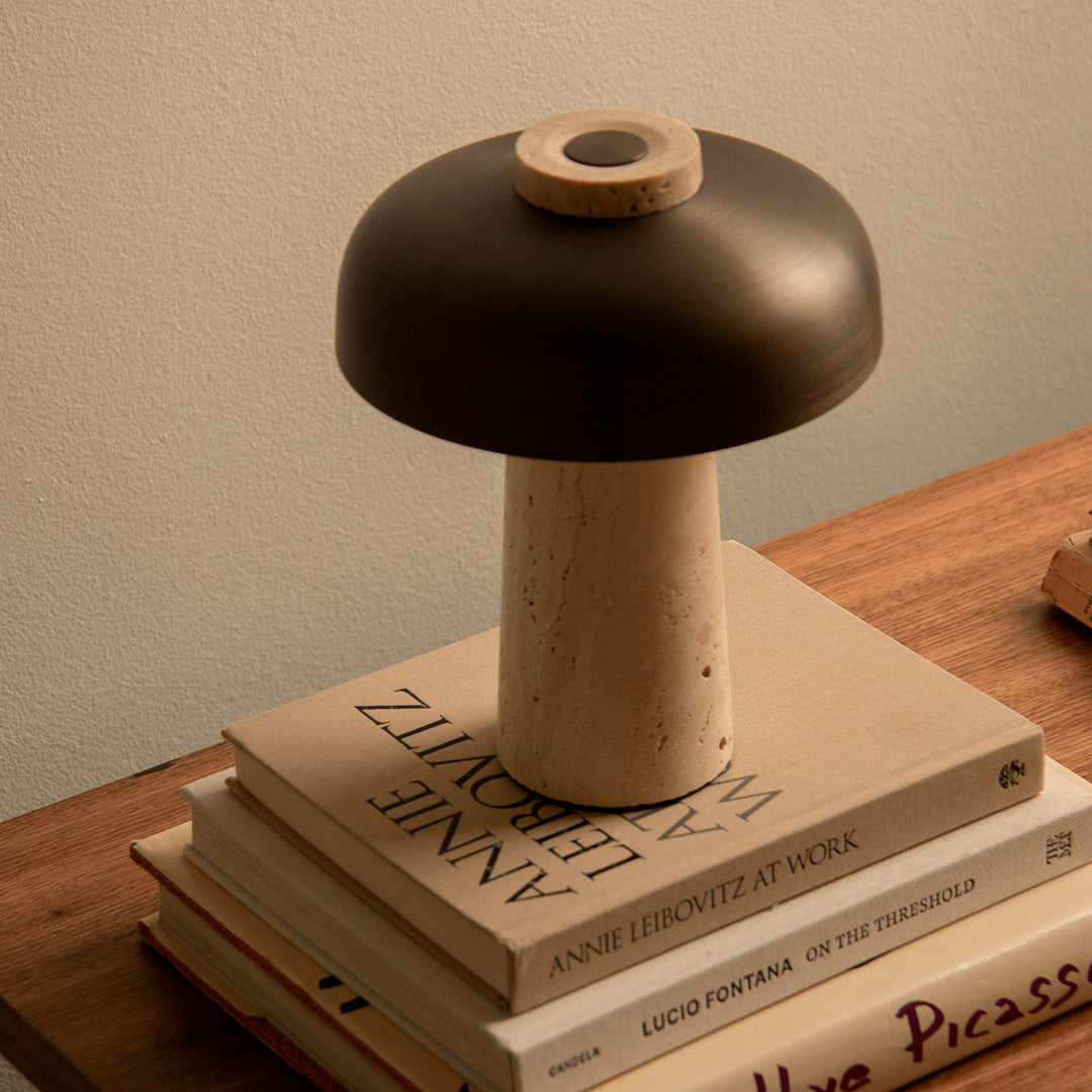 Modern mushroom lamp with a matte black hood and a beige stone base, resting atop stacked books.