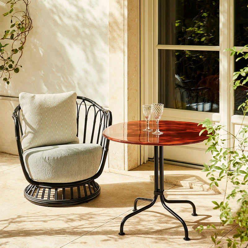 Black wicker chair with soft blue cushion and red circular table top, set against a neutral outdoor backdrop.