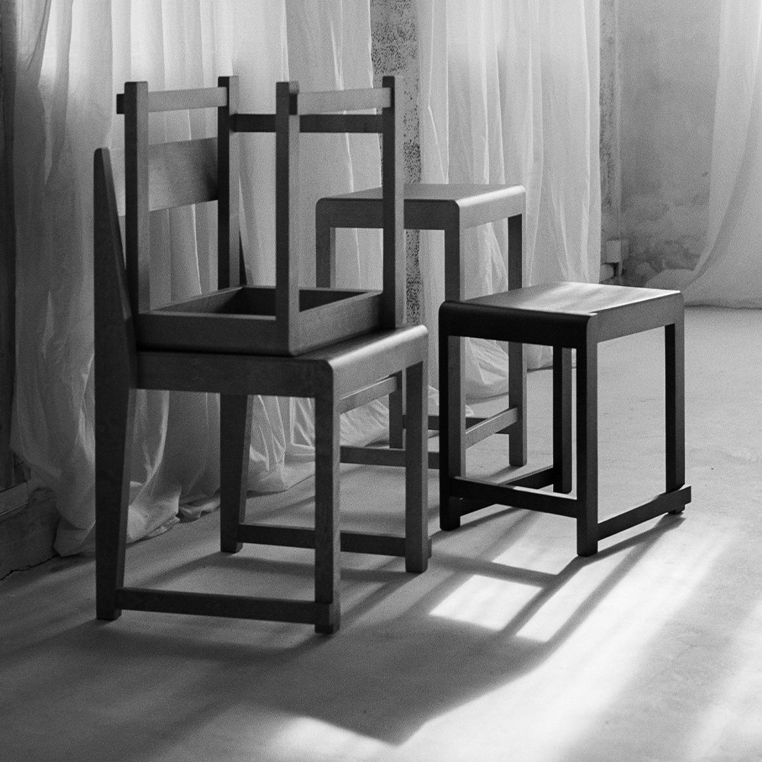 Black and gray wooden chairs with simple, modern designs and smooth surfaces. Soft shadows create depth.