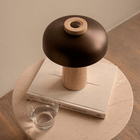 Modern lamp with a sleek black shade and a light wood base, styled on a textured book and light-colored tabletop.