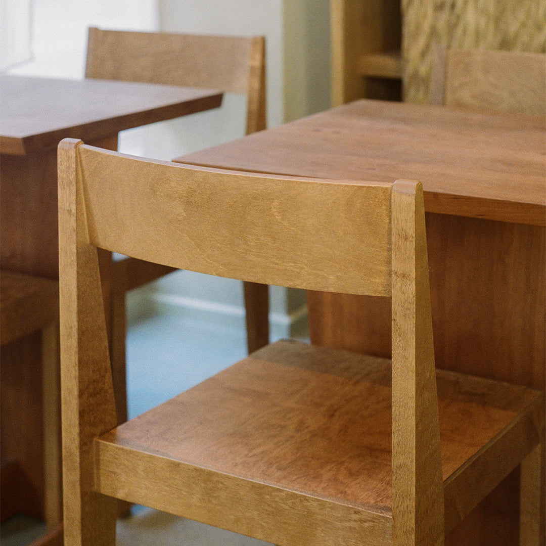 Light brown wooden chair with a smooth finish, complemented by matching wooden table. Simple and modern design.