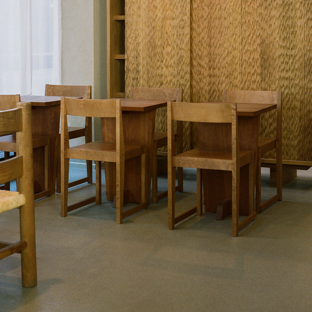 Natural wood dining chairs in a neutral-toned room with textured woven walls and a minimalist, earthy aesthetic.