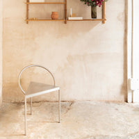 Sleek metallic silver chair with a minimalist triangular design, set against a neutral textured wall.
