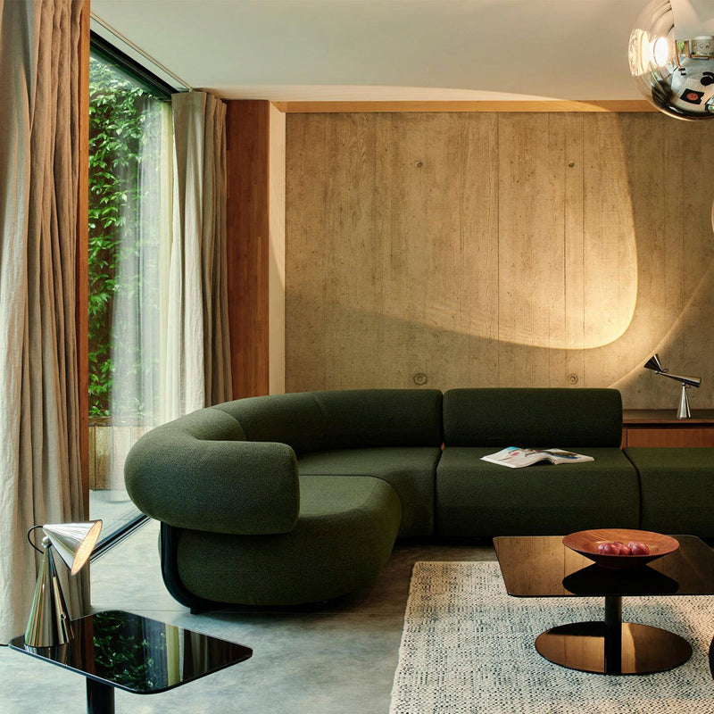 Green curved sofa with textured fabric, natural wood accents, and a black glossy table against a concrete wall.