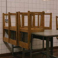Wooden chairs stacked on a gray table against a white tiled wall, featuring a simple, minimalist design.