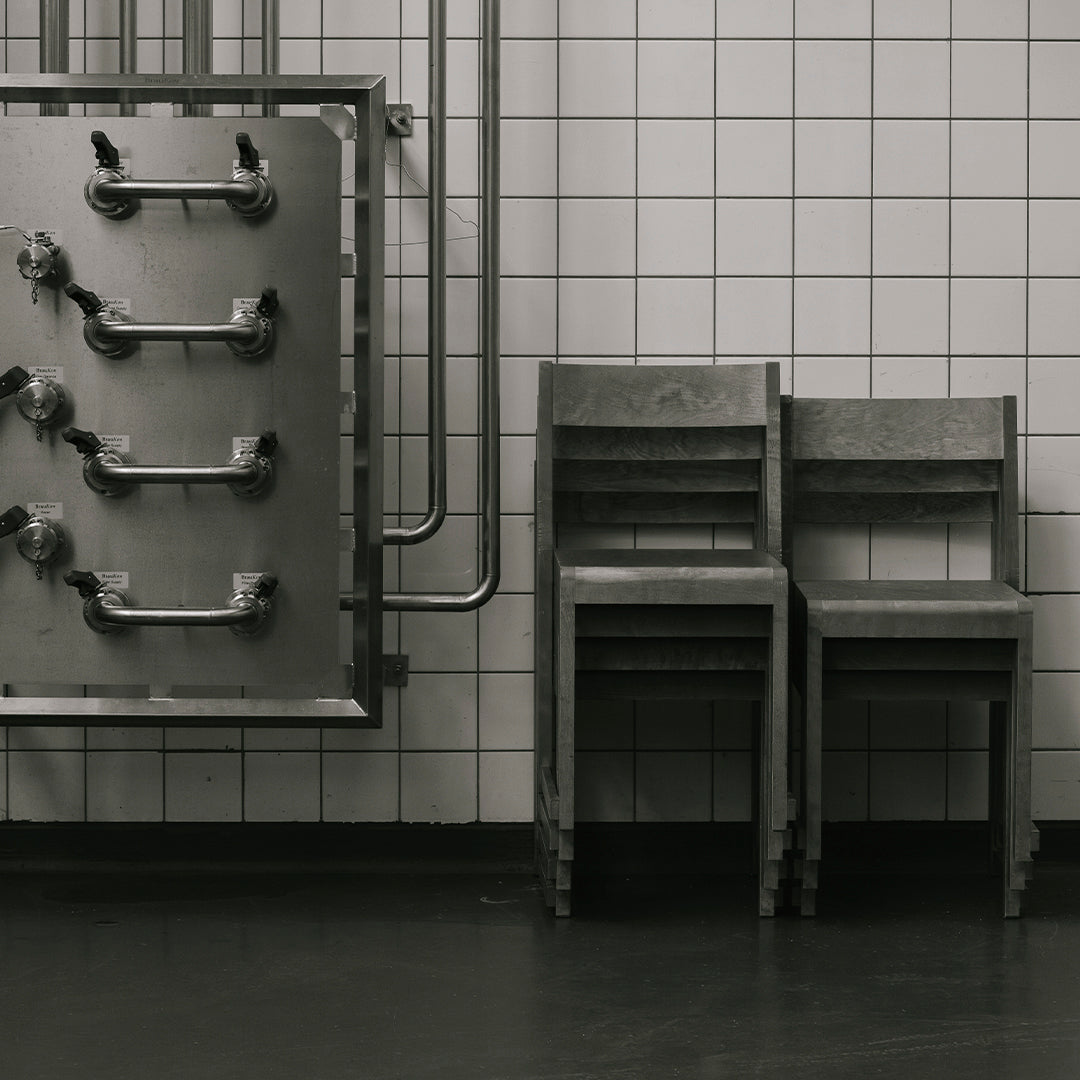 Gray metal chair set against a white tiled wall, featuring industrial pipes for a minimalist, modern aesthetic.