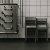 Gray metal chair set against a white tiled wall, featuring industrial pipes for a minimalist, modern aesthetic.