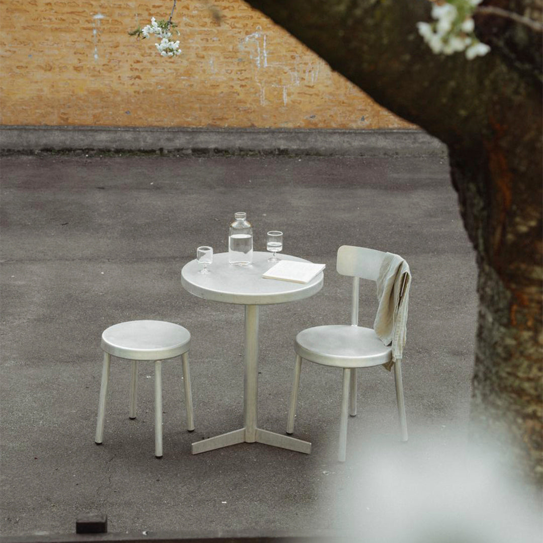 Minimalist white round table and two chairs on a textured gray surface, accented by a natural backdrop.