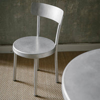 Silver metal chair with a smooth, sleek finish against a textured neutral background.