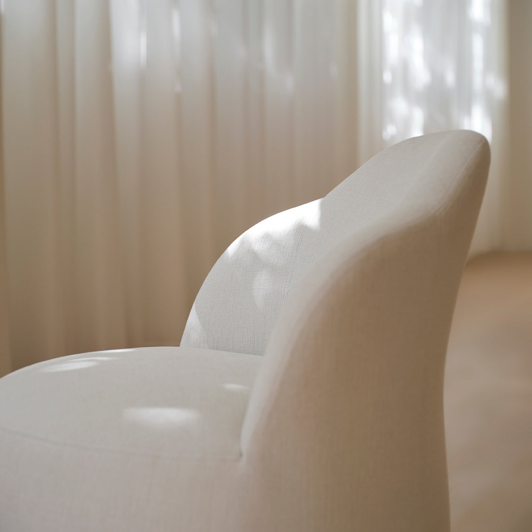 Soft cream chair featuring a textured fabric with gentle curves, illuminated by diffused natural light.