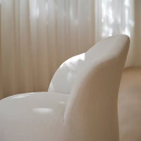 Soft cream chair featuring a textured fabric with gentle curves, illuminated by diffused natural light.