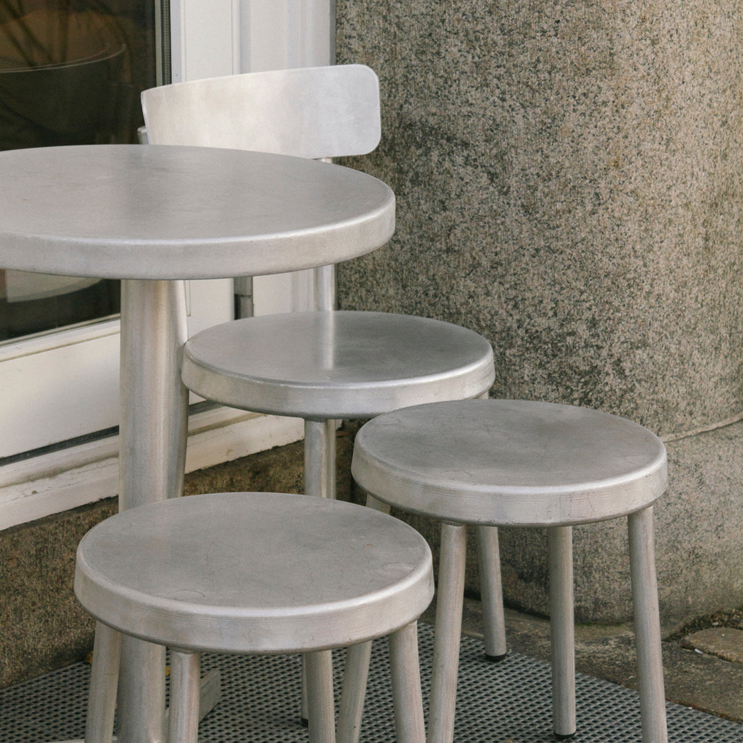 Silver metal table and stools with sleek, minimalist design, featuring smooth surfaces and geometric shapes.