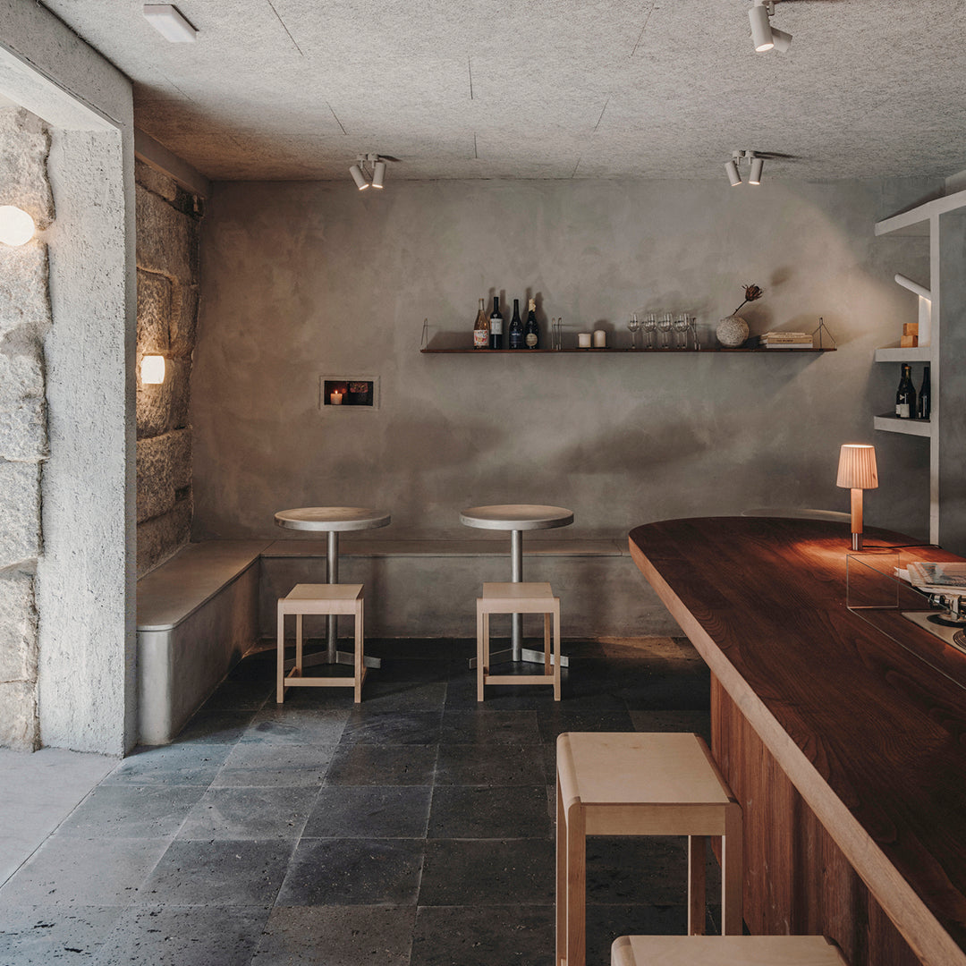 Modern bar interior featuring neutral tones, warm wood accents, and minimalist design with stone flooring and soft lighting.