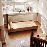 Beige minimalist daybed with light wood accents, featuring a smooth, solid surface and cylindrical cushion.