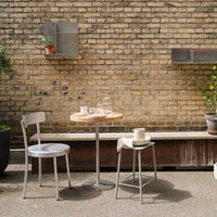 "Light gray metal chair and table set with natural wood top, surrounded by a warm brick wall and greenery."