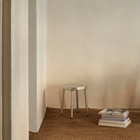 Silver metal stool against a neutral wall, with earthy tones from stacked books and natural woven rug.