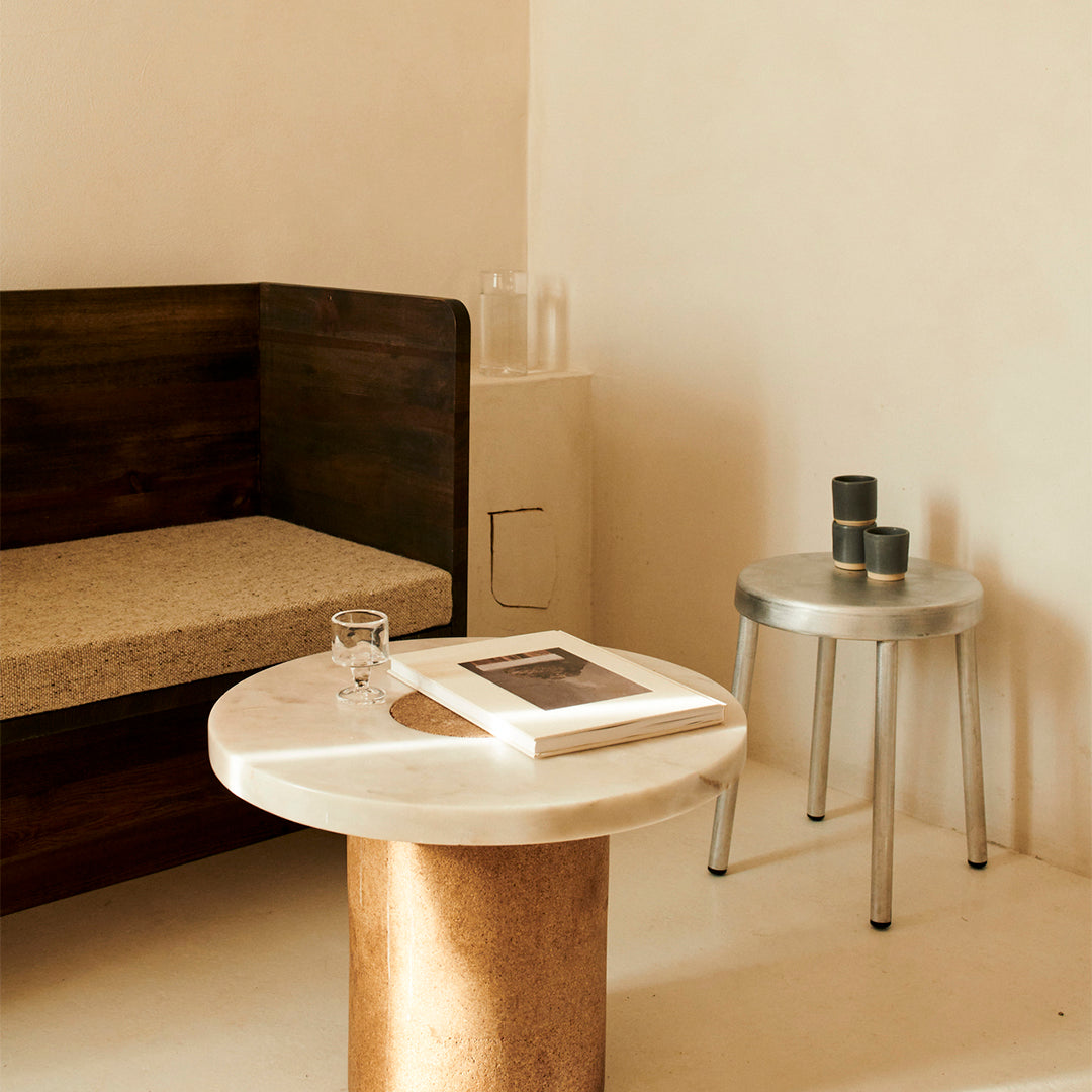 "Marble table with circular top and cork base, complemented by a sleek silver stool in a warm-toned interior."