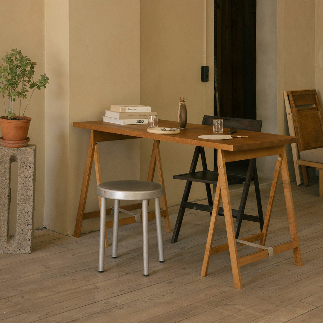 Wooden table with natural finish, gray metal stool, black and silver accents, and warm earthy tones in a minimalist setting.