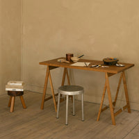 Wooden table with natural finish, silver metal stool, and warm beige wall, creating a minimalist aesthetic.