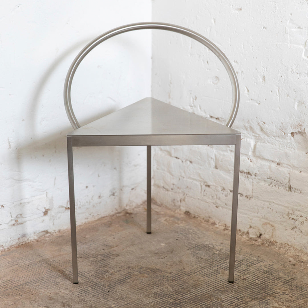 Triangular metal chair with a sleek silver finish and minimalist circular backrest design.