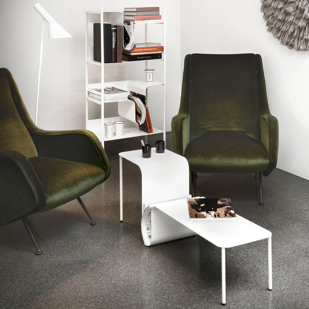 Modern living room with green armchairs, a white side table, and a bookshelf.