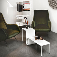 Modern living room with green armchairs, a white side table, and a bookshelf.