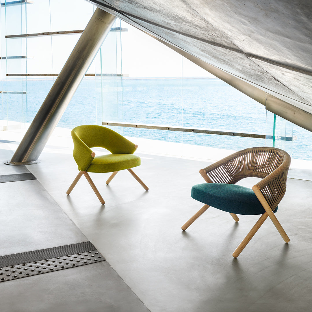 Two modern chairs in vibrant lime green and deep teal, featuring unique patterns and natural wood legs, against a coastal backdrop.