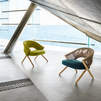Two modern chairs in vibrant lime green and deep teal, featuring unique patterns and natural wood legs, against a coastal backdrop.
