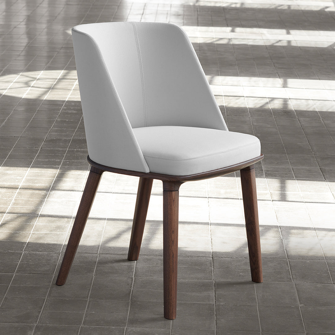 Modern white chair with smooth upholstery and dark wooden legs, set against a textured grey floor backdrop.