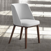 Modern white chair with smooth upholstery and dark wooden legs, set against a textured grey floor backdrop.