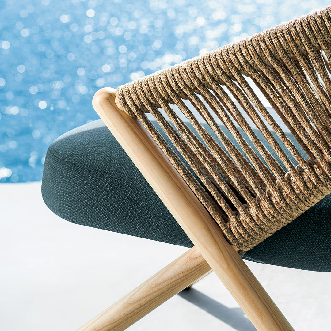 Natural wood chair with beige rope detailing and a deep green upholstered seat, set against a blue water backdrop.