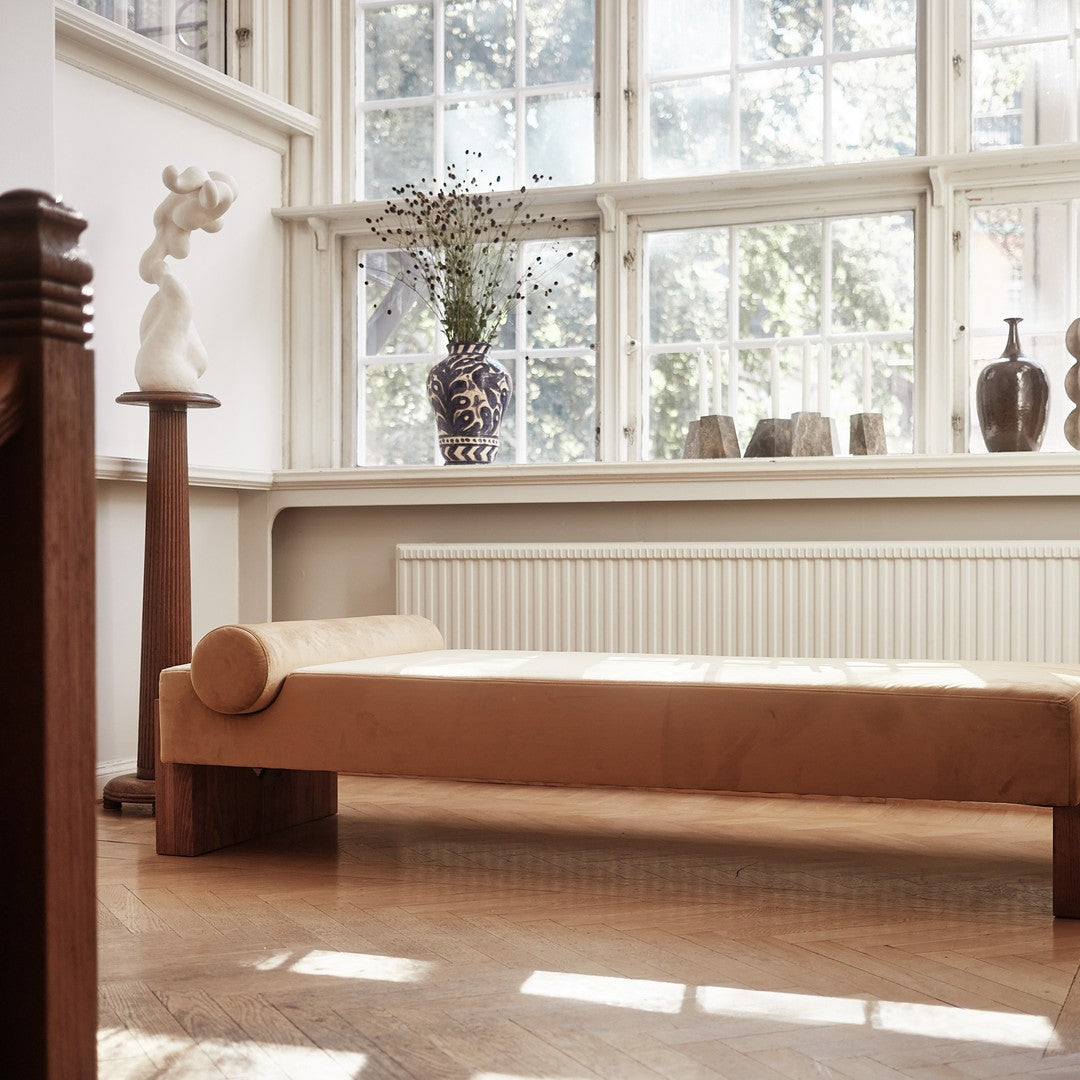 "Modern beige chaise lounge with a textured finish, set against a bright, airy room filled with natural light."