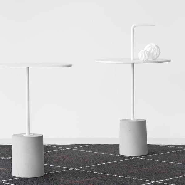 Modern white side tables with gray bases on a dark patterned rug featuring grid lines and accents in red and orange.