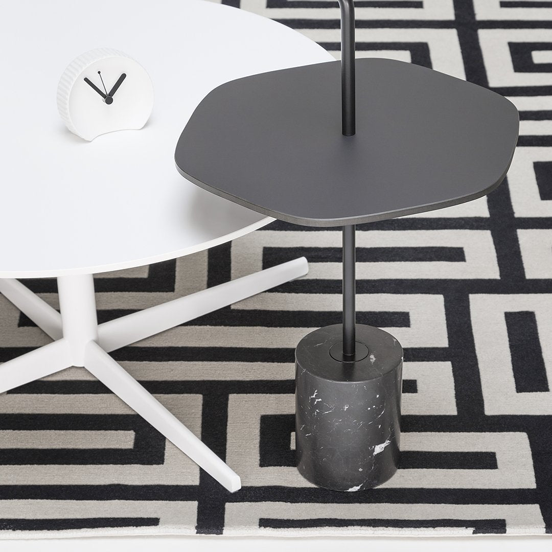 Modern hexagonal gray table with a black base on a black and white geometric patterned rug. Clean and stylish design.
