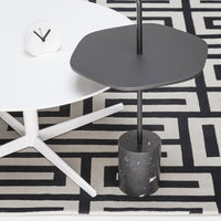 Modern hexagonal gray table with a black base on a black and white geometric patterned rug. Clean and stylish design.