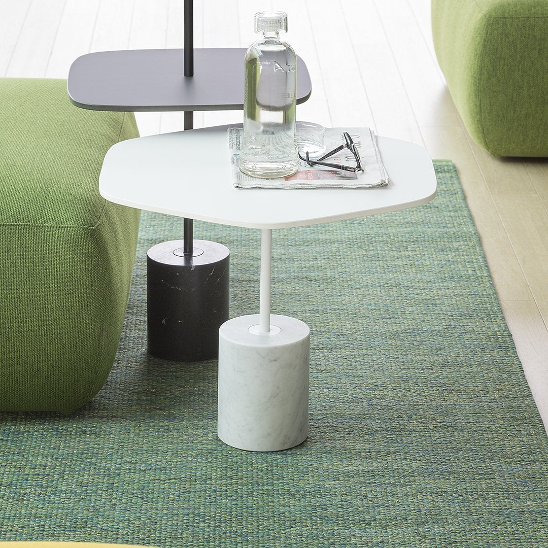 Geometric side tables in black, white, and gray with a textured green rug background. Modern design elements.