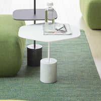 Geometric side tables in black, white, and gray with a textured green rug background. Modern design elements.