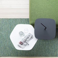 Stylish hexagonal side table with a sleek black top and white base, set against a textured green rug.