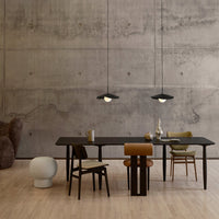 Modern dining space featuring a black table, earthy-toned chairs, and soft gray concrete walls. Elegant pendant lighting above.