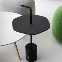 Black hexagonal side table with a marble base and minimalist design, complemented by soft gray and green furniture.