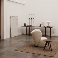 Cream textured chair on a brown woven rug, against muted gray stone floor and minimalist white walls.